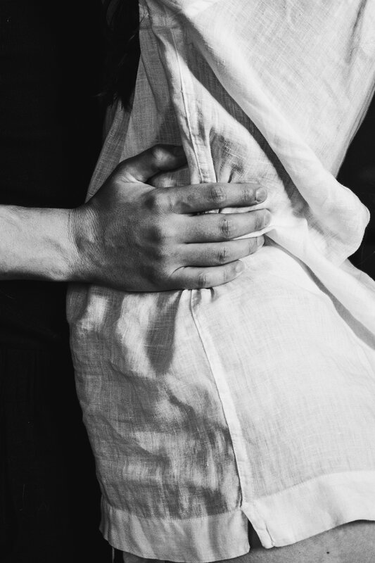 Dettaglio in bianco e nero: mani che si stringono sulla schiena, camicia di lino