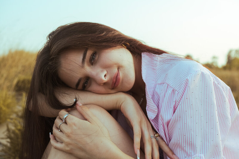 Ragazza distesa nell'erba alta al tramonto, camicia a righe